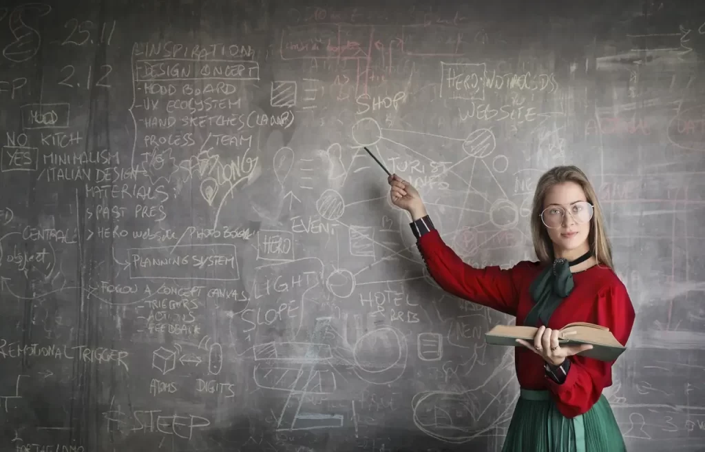 A female teacher pointing to the blackboard.