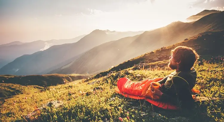 A man in a sleeping bag watches the surrounding view.