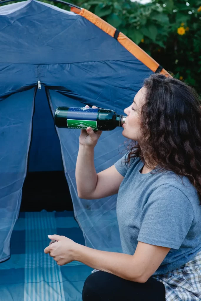 A woman drinking water in front of her tent.